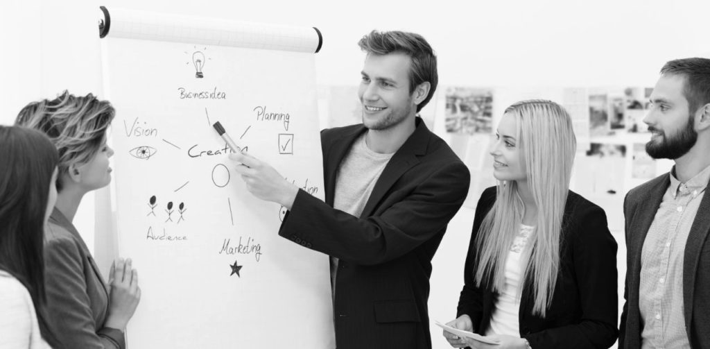 Manager présentant un schéma au paperboard devant trois collègues