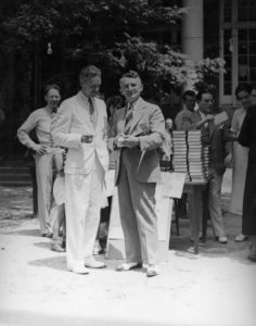 Dale Carnegie en costume clair, en extérieur, devant des piles de livres